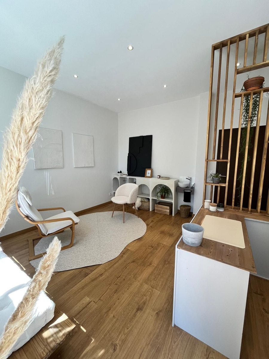 Le cabinet des 3 fontaines : un fauteuil et une chaise en tissu bouclé autour d'un tapis clair, parquet en bois et claustra en bois